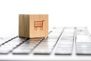 Cubo de madera con dibujo de carrito de compras sobre teclado de una laptop